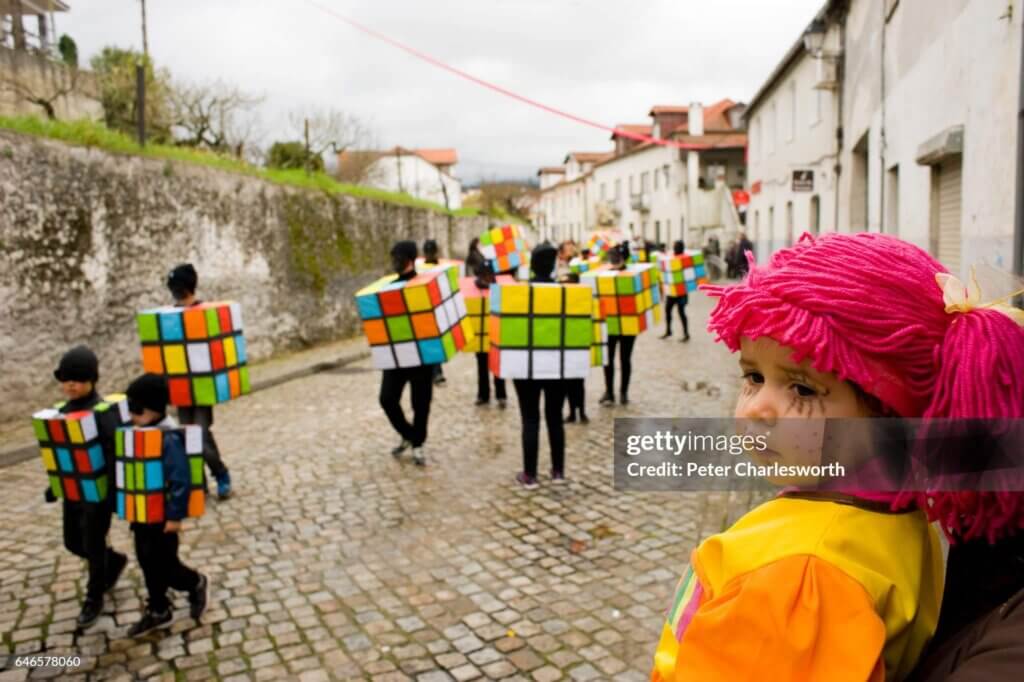 A dressed up girl watches people dressed as Rubik's cubes...COJA, ARGANIL, PORTUGAL - 2017/02/28: A dressed up girl watches people dressed as Rubik's cubes parade in the carnival procession through the main street of the mountain town of Coja. (Photo by Peter Charlesworth/LightRocket via Getty Images)