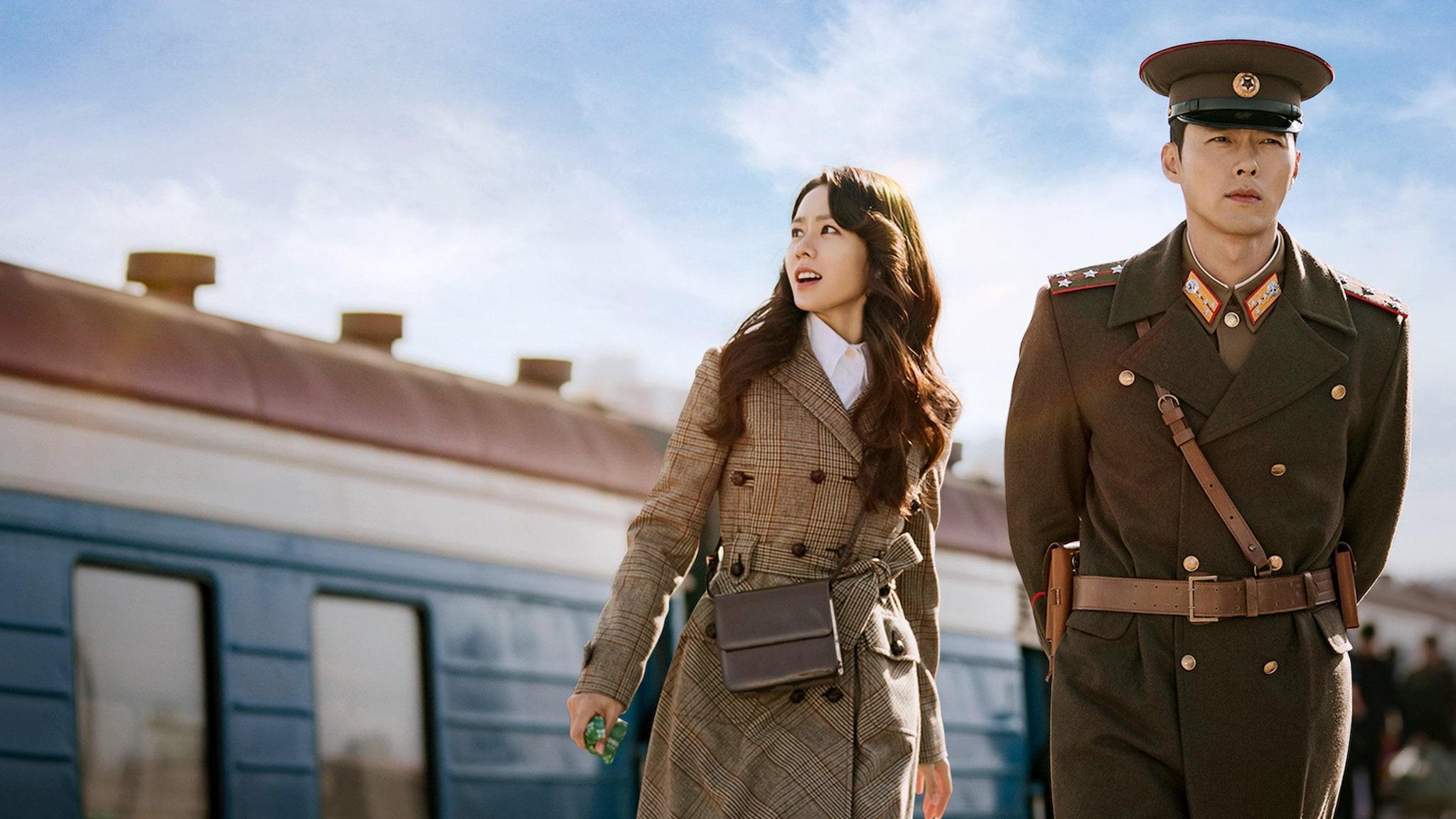 Main characters in military attire standing by a train for drama poster.