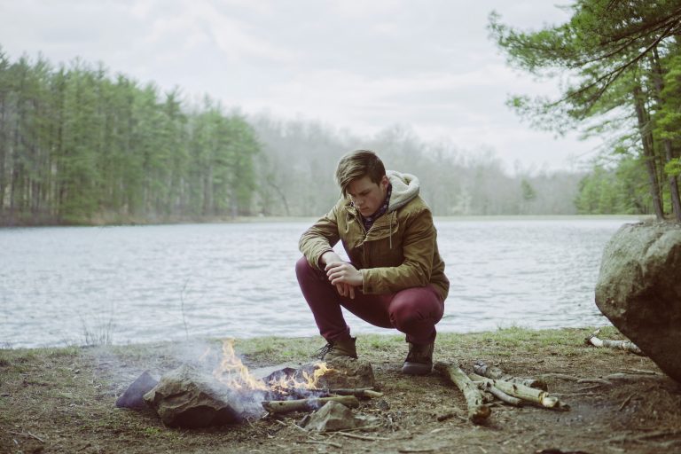 Alone Time: man with campfire by a lake in the woods.