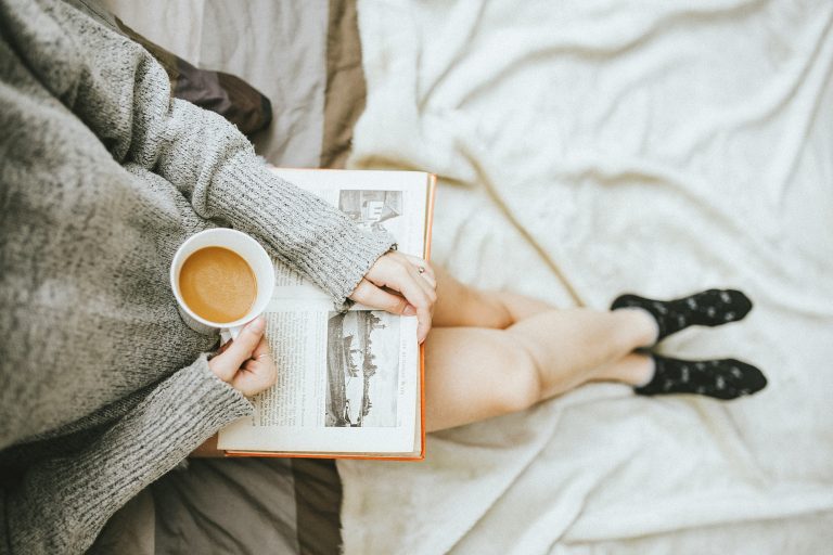 Image used for our must-reads list. A woman enjoying self-care Sunday, engrossed in a book while lying on her bed. Photo by Anthony Tran on Unsplash.com. https://unsplash.com/photos/woman-holding-a-cup-of-coffee-at-right-hand-and-reading-book-on-her-lap-while-holding-it-open-with-her-left-hand-in-a-well-lit-room-8i2fHtStfxk