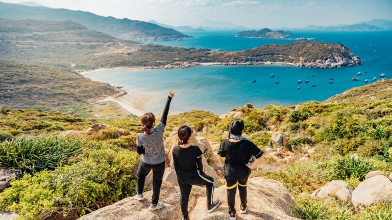 Three people on a cliff. This is the featured image for the article on vacation spots to take your mom to. Image courtesy of Unsplash.com. https://unsplash.com/photos/three-women-on-mountain-JsuBKjHGDMM