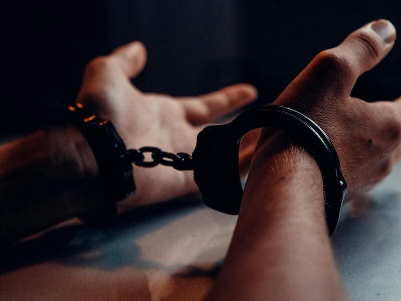 Photo by Kindel Media: https://s://www.pexels.com/photo/a-person-s-hands-on-the-table-wearing-handcuffs-7773260/