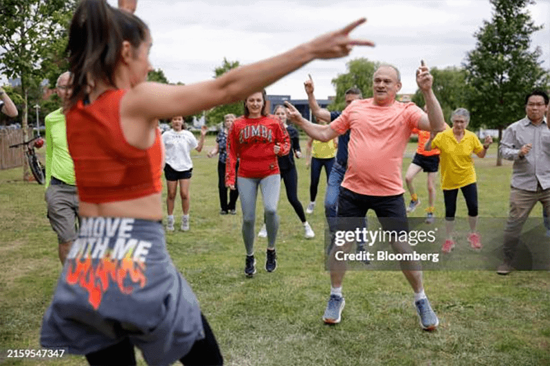 A Zumba instructor leading a class outdoors in a green field.