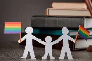 happy-gay-couple-with-child-rainbow-lgbt-flags-paper-people-chain with books covering lgbtq material you can check out in Queer Liberation Library