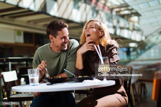 Happy young couple laughing while having lunch at a food court- Relationship myths