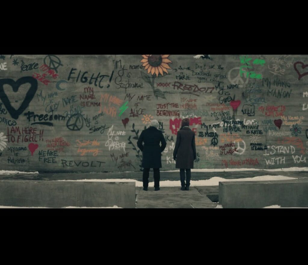 June (Elisabeth Moss) and Emily (Alexis Bledel) stand in front of a wall of celebratory graffiti.