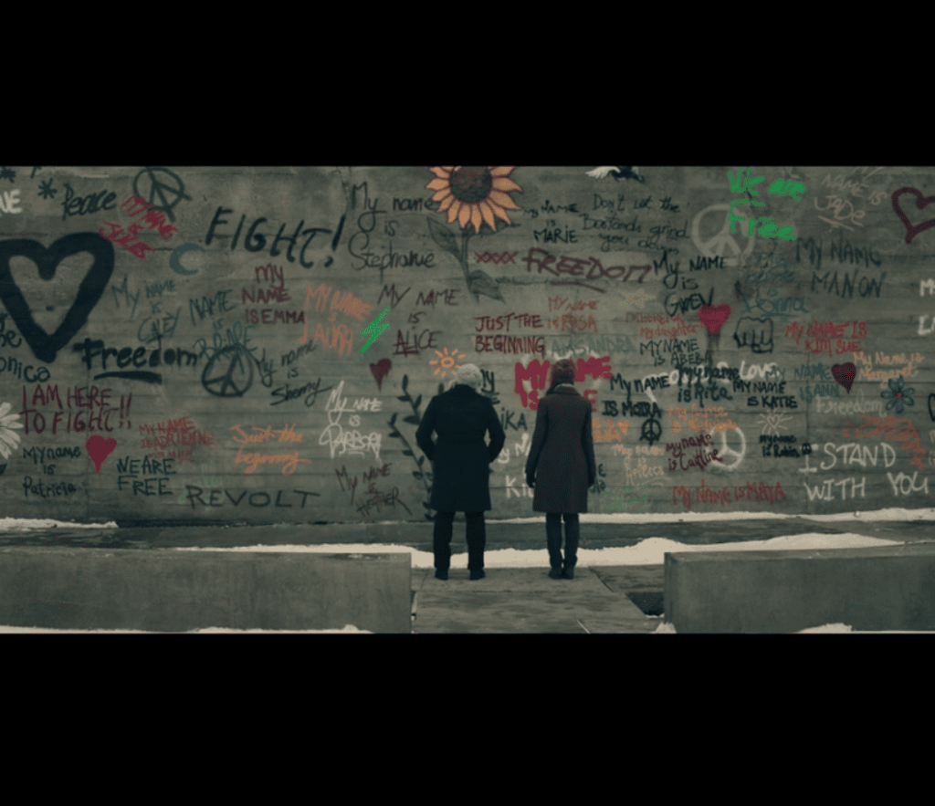 June (Elisabeth Moss) and Emily (Alexis Bledel) stand in front of a wall of celebratory graffiti.