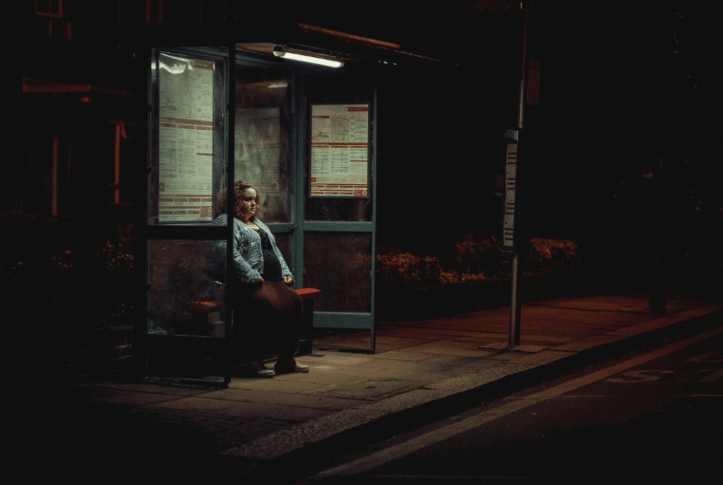 A lonely woman waits at a dimly lit bus stop in a tense scene from the Netflix show Baby Reindeer.