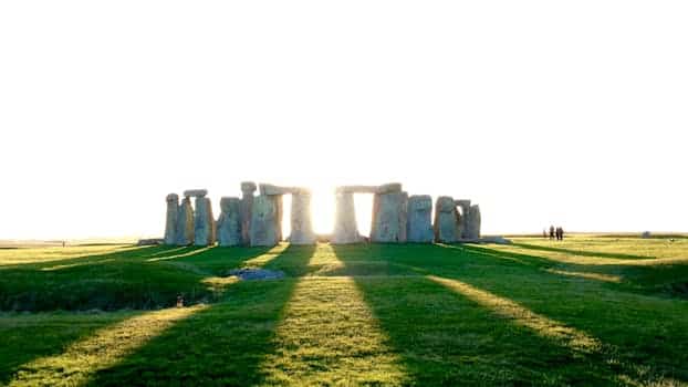 Explore the iconic Stonehenge under the bright sunlight casting long shadows across the grass. Summer Solstice