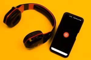 Wireless headphones and smartphone with play icon on a vibrant yellow background. Top 10 streaming artists on YouTube Music