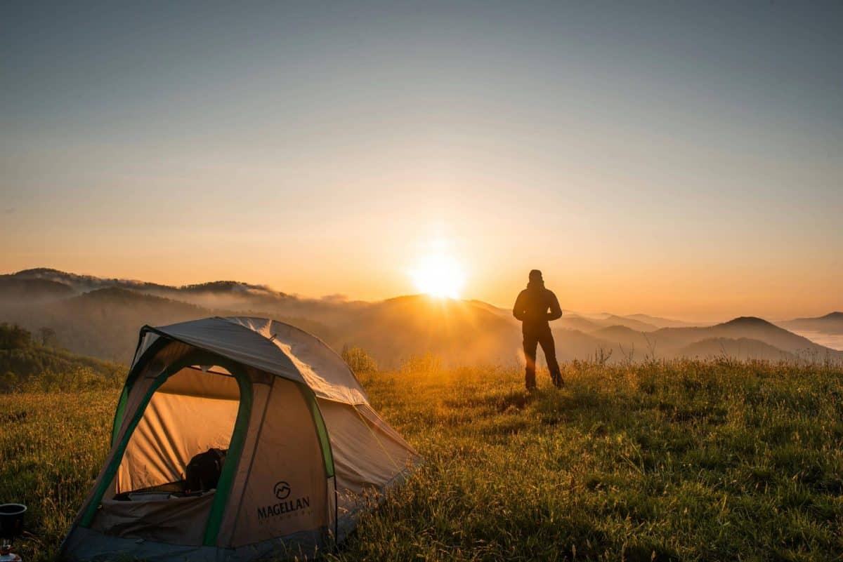 A camper enjoys the sunrise in a mountain setting with a tent. Perfect nature escape. non-beach destination. non-beach destinations.