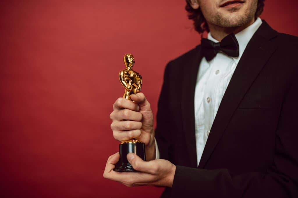 Elegant man in tuxedo holding a gold trophy against a red background, celebrating an achievement.
