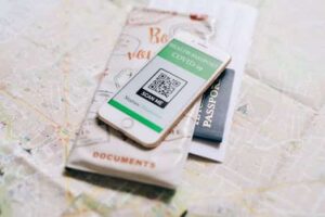 A smartphone displaying a COVID-19 health passport on a map with a travel passport. 1Password