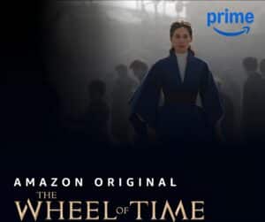 Screenshot of a promotional image from the tv show The Wheel of Time. Character in a blue coat and white turtleneck.