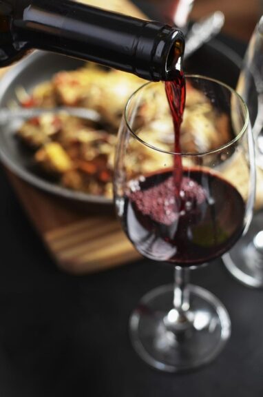 A bottle of red wine pouring into a glass during dinner, with a warm, elegant table setting in the background.