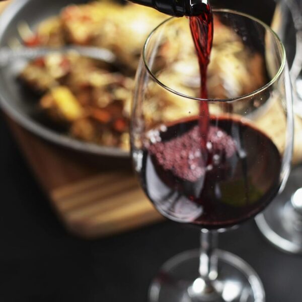 A bottle of red wine pouring into a glass during dinner, with a warm, elegant table setting in the background.