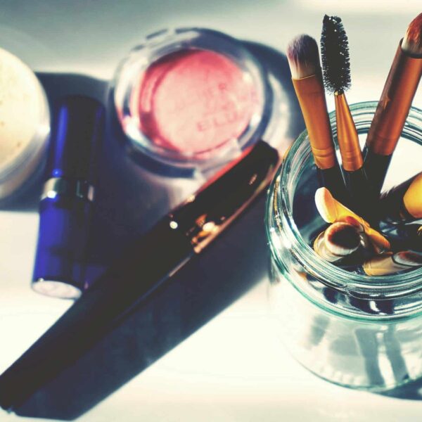 Artistic flat lay of makeup brushes in a jar surrounded by colorful cosmetics, perfect for beauty themes. June beauty launches