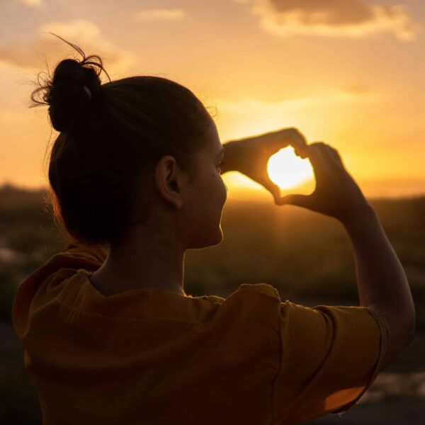 A silhouette of a young woman forming a heart shape at sunset in Kelâat M'Gouna, Morocco. summer solstice