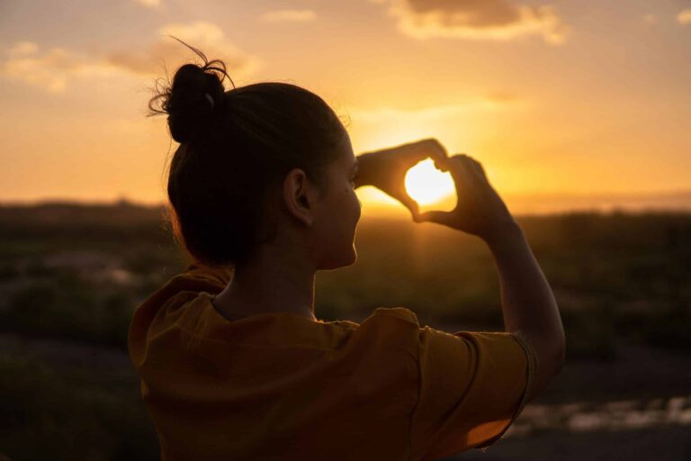 A silhouette of a young woman forming a heart shape at sunset in Kelâat M'Gouna, Morocco. summer solstice
