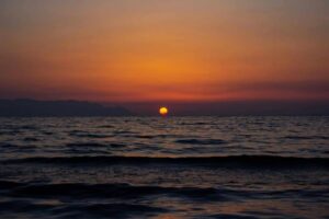 A breathtaking sunset over the ocean with a vibrant orange sky and gentle waves. summer solstice
