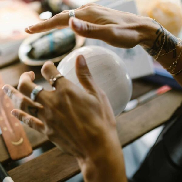 A close-up of hands with jewelry interacting with a mystical crystal ball on a wooden table. spirituality, new moon, new moon in cancer