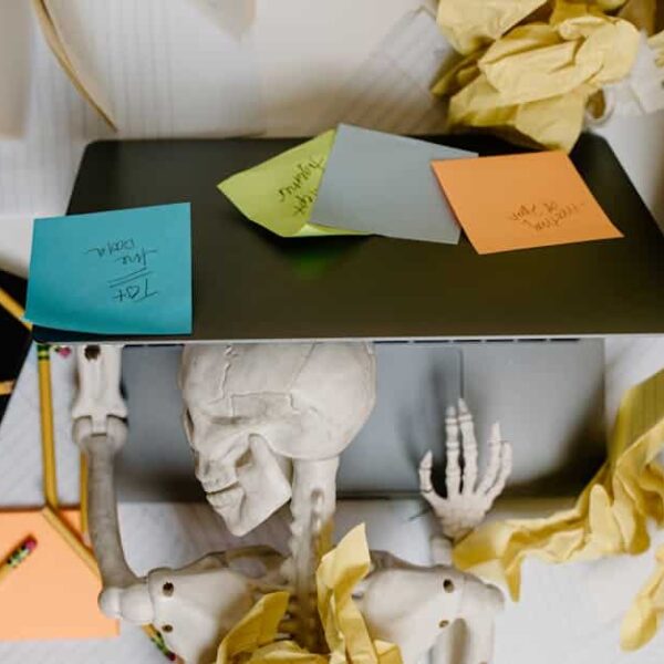 Skeleton at a laptop surrounded by notes and paper, symbolizing work burnout and the need for a digital detox.