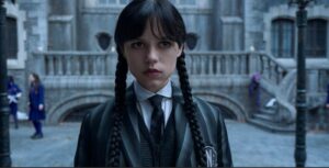 Jenna Ortega as Wednesday Addams, with braided pigtails and a serious expression, wearing her school uniform. Season 3