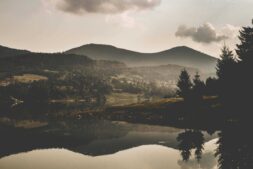 Fog palette tones define this serene mountain scene—misty peaks, soft lake reflections, and a cloudy sky create a calm, dreamlike mood. Image by Vlad Bagacian in Courtesy of Pexel