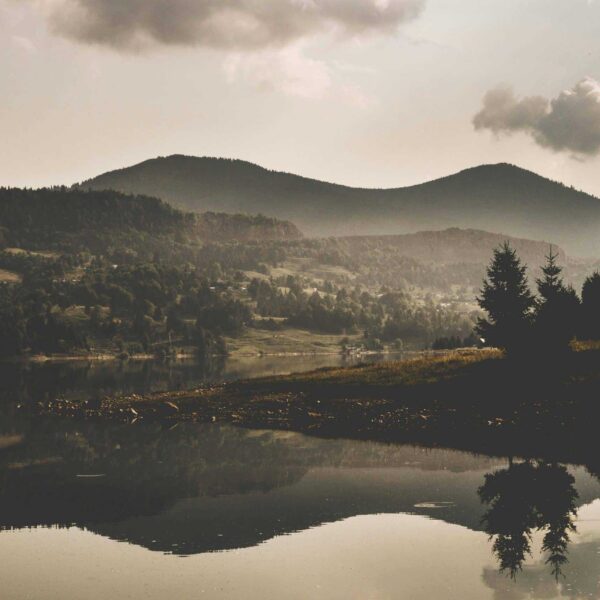 Fog palette tones define this serene mountain scene—misty peaks, soft lake reflections, and a cloudy sky create a calm, dreamlike mood. Image by Vlad Bagacian in Courtesy of Pexel