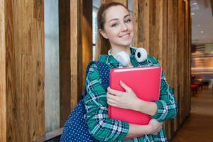 Smiling student holding book and wearing headphones, ready for study. college students