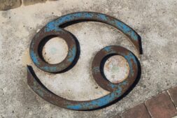 Close-up of a rusted Cancer zodiac symbol on a concrete wall. Venus in Cancer