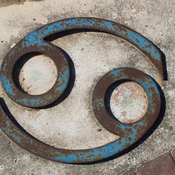 Close-up of a rusted Cancer zodiac symbol on a concrete wall. Venus in Cancer