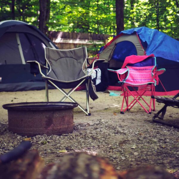 A serene campsite in the woods with colorful tents, camping chairs, and a fire pit, perfect for a leisure getaway.