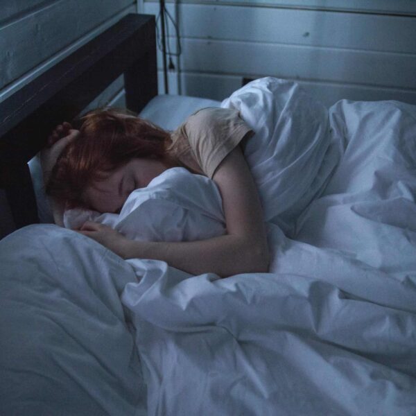 A woman sleeping peacefully in a cozy bedroom, enveloped by soft white sheets, under the gentle glow of night lighting. sleep supplements