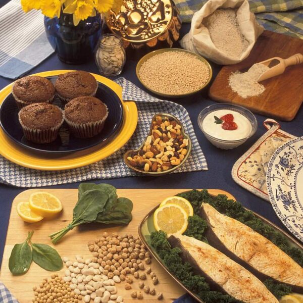 Plant-based foods rich in magnesium—bran muffins, pumpkin seeds, barley, buckwheat flour, yogurt, halibut, chickpeas, soy, spinach—arranged on a spring-themed presentation table with floral decor. Image by FotoshopTofs via Pixabay.