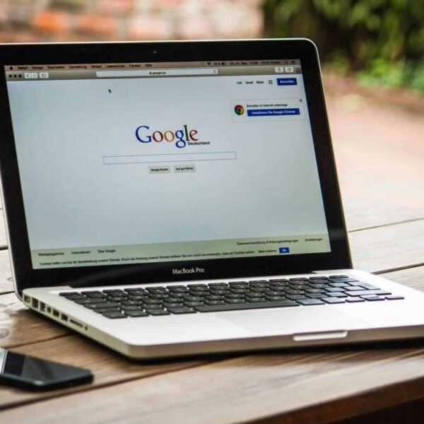 A MacBook Pro displaying Google Search on a wooden table outdoors, next to a smartphone. Faith, social media