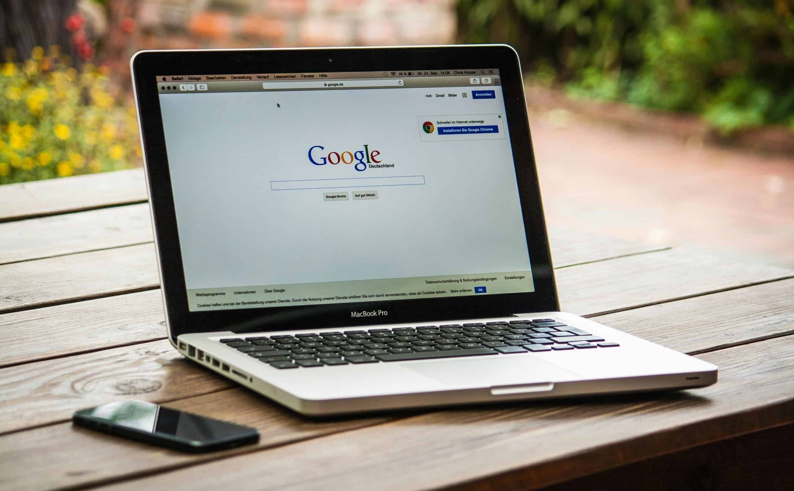 A MacBook Pro displaying Google Search on a wooden table outdoors, next to a smartphone. Faith, social media
