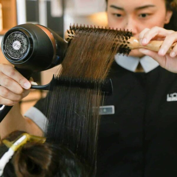 Hairdresser expertly styles hair using a brush and dryer in a salon setting. haircare tools
