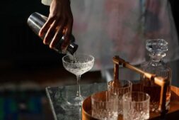 A bartender pours a cocktail into a glass from a shaker, set in a cozy home bar.