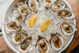 flesh-eating bacteria, A bowl of fresh oysters on ice garnished with lemon wedges, showcasing seafood freshness.
