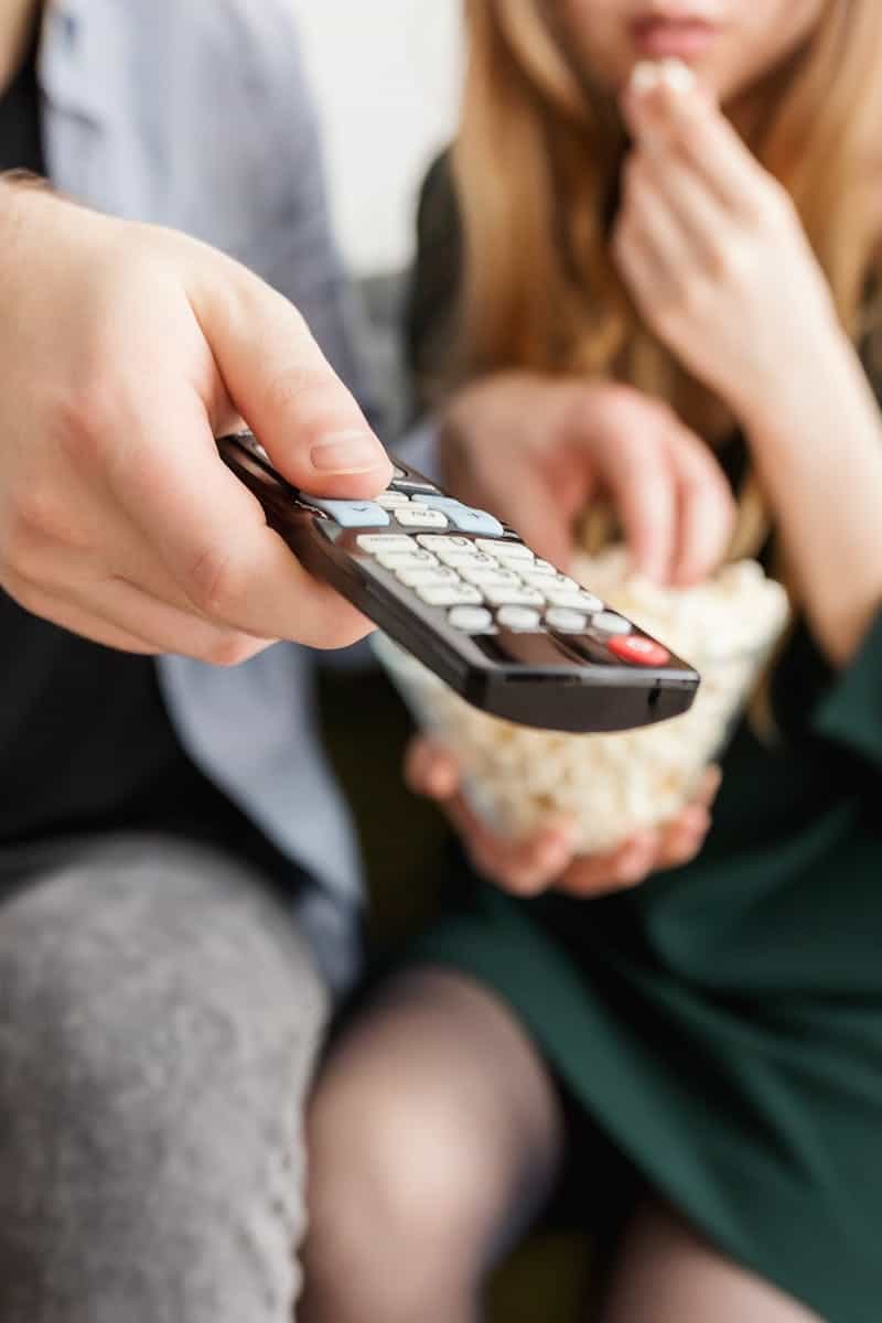 A couple enjoying a relaxing movie night, sitting on a sofa with popcorn and a TV remote.