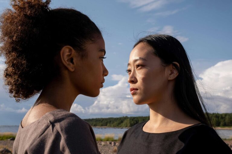 A close-up outdoor portrait of two women facing each other under a bright sky. toxic friendship