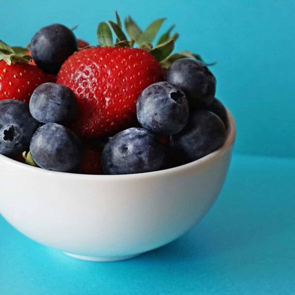 A vibrant mix of fresh strawberries and blueberries in a white bowl on a blue background.