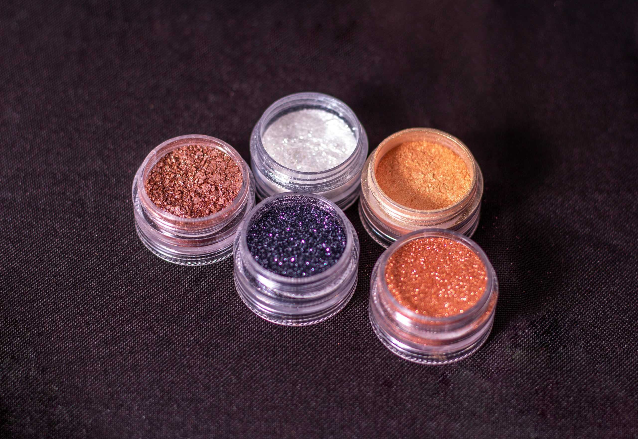 Close-up of assorted cosmetic glitters in round containers on a dark background. Makeup hacks