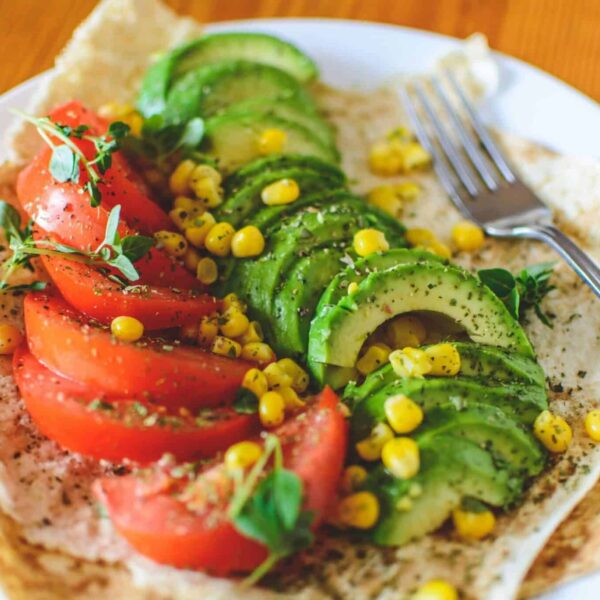 A vibrant salad vegan meals with avocado, tomato, and corn on flatbread, topped with herbs, perfect for a healthy meal.