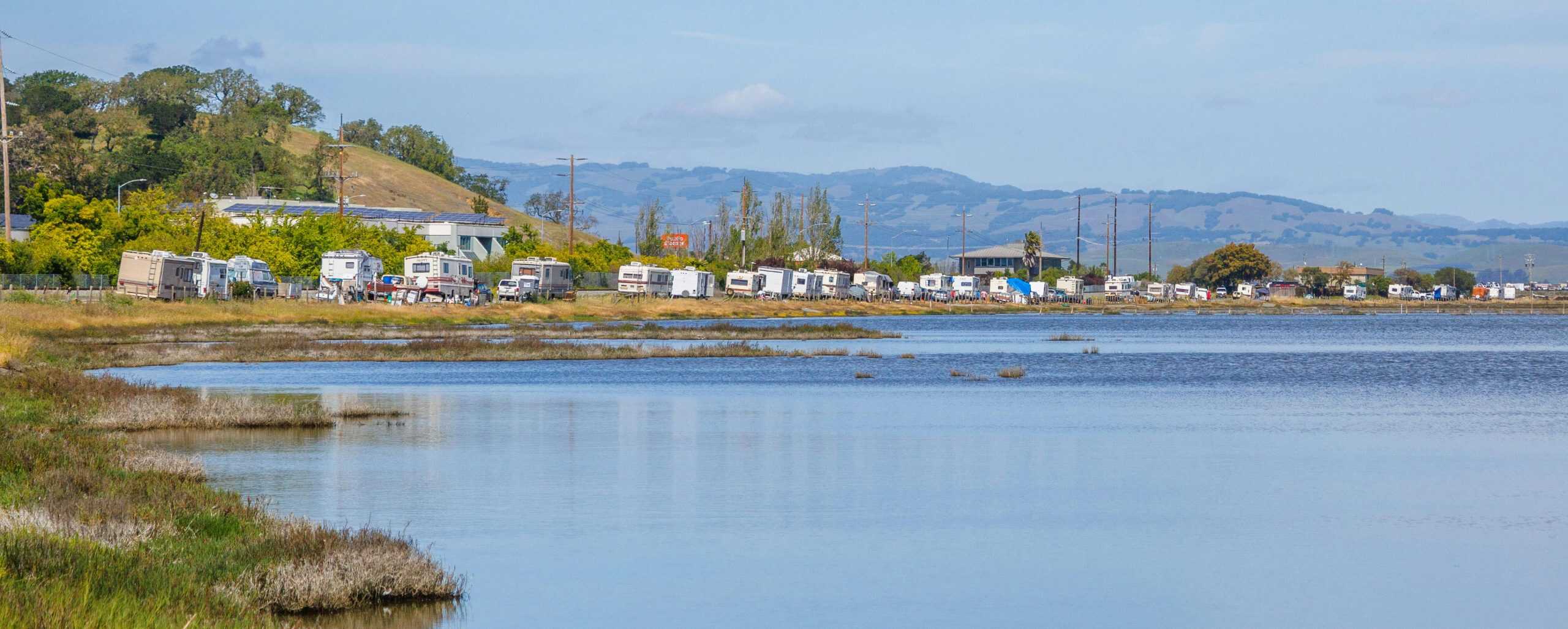 Tranquil RV site by the lake with beautiful mountain backdrop and clear blue skies.