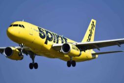 Yellow Spirit Airlines aircraft captured mid-air against a clear blue sky.