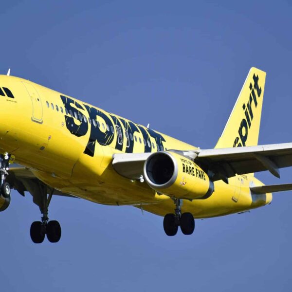 Yellow Spirit Airlines aircraft captured mid-air against a clear blue sky.