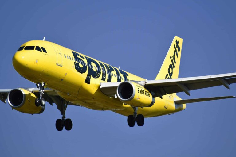 Yellow Spirit Airlines aircraft captured mid-air against a clear blue sky.