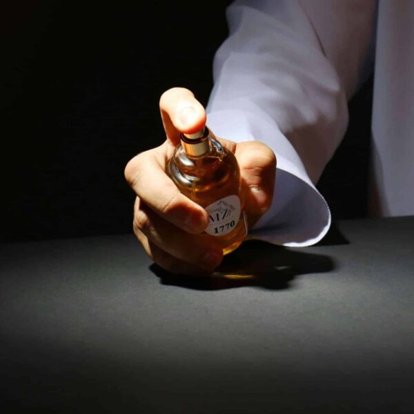 A hand elegantly holding a perfume bottle against a dark backdrop, highlighting luxury fragrance. Colognes